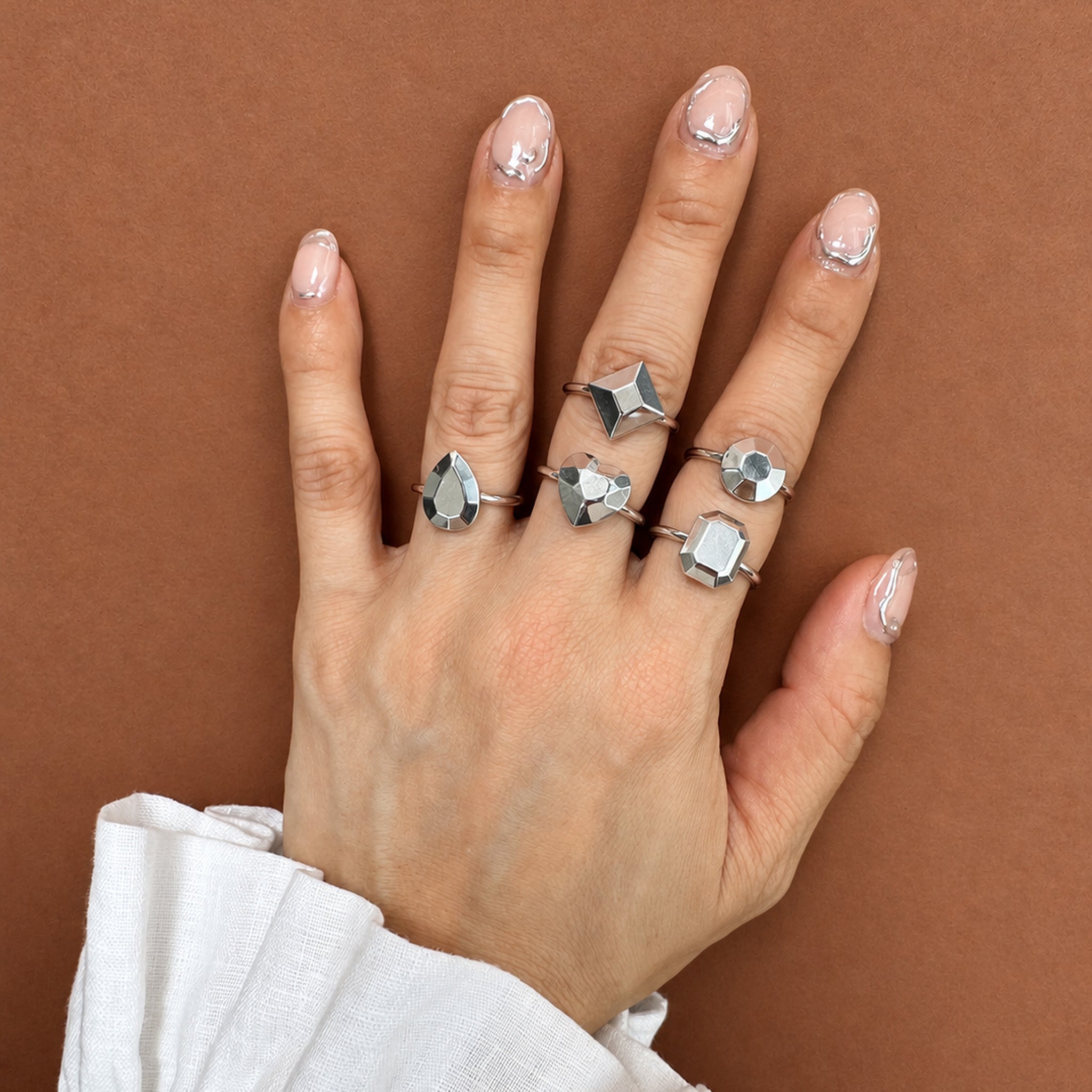 A hand wearing five silver rings with geometric, faceted star and cube-like designs by Jennifer Loiselle