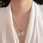 Silver necklace with a horse pendant worn by a person in a white outfit.