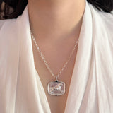 Silver necklace with a horse pendant worn by a person in a white outfit.